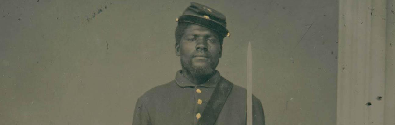 黑白照片的黑人士兵站在立正，拿着一把剑旁边的柱子